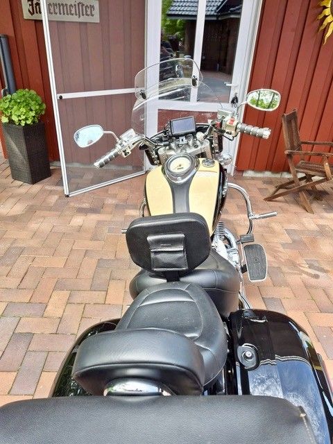 Ein schwarzes Motorrad parkte auf einer gemauerten Terrasse vor einem Ladenlokal mit offenen Glastüren.
