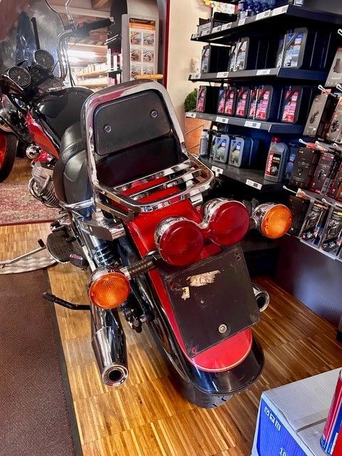 Schwarzes Motorrad mit roten Rücklichtern und offenem Sitz in einem Ausstellungsraum, umgeben von Regalen und anderen Motorrädern.