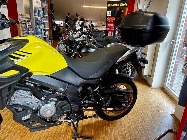 Ein gelb-schwarzes Motorrad steht in einem Ausstellungsraum neben einer Glastür und anderen Motorrädern.