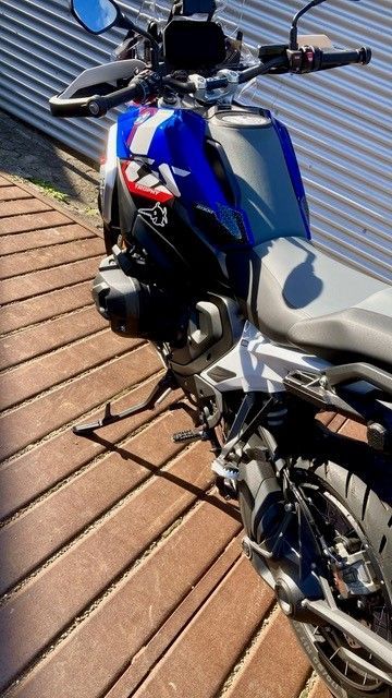 Auf einem Holzdeck ist ein blau-rotes Motorrad geparkt.