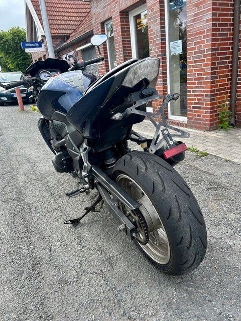 Schwarzes Sportmotorrad, geparkt neben einem Backsteingebäude auf einer Schotterauffahrt, Ansicht von hinten.