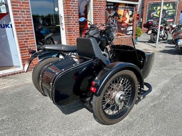 Schwarzes Motorrad mit Beiwagen, vor einem Backsteingebäude geparkt.