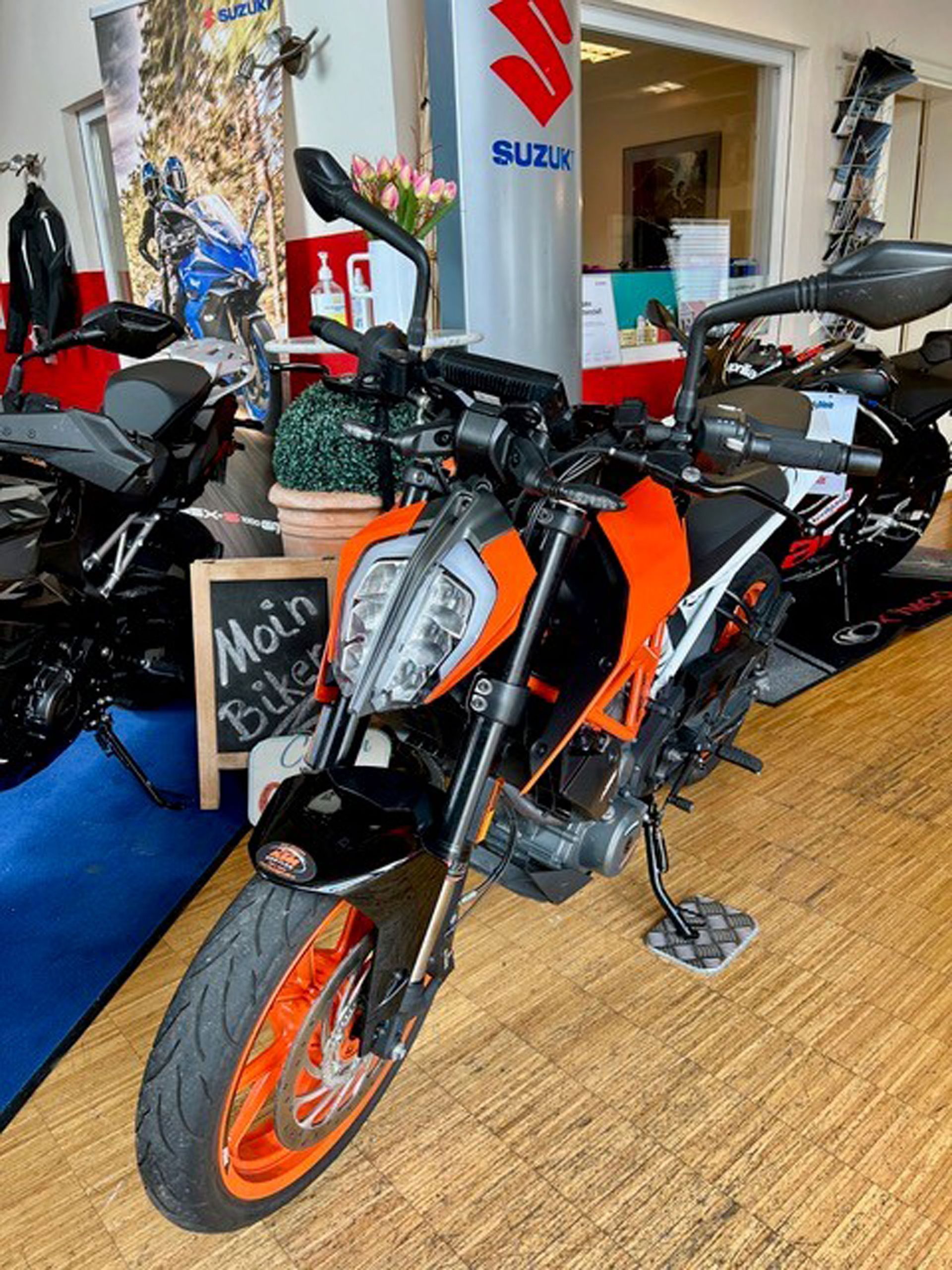 Orange-schwarzes KTM Duke-Motorrad in einem Laden ausgestellt. Das Motorrad steht auf einem Holzboden.