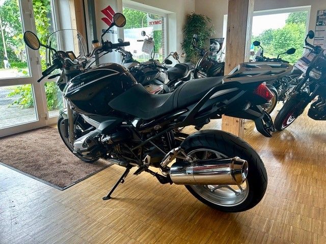 Schwarzes Sportmotorrad in einem Ausstellungsraum mit großen Fenstern und anderen Motorrädern in der Nähe.