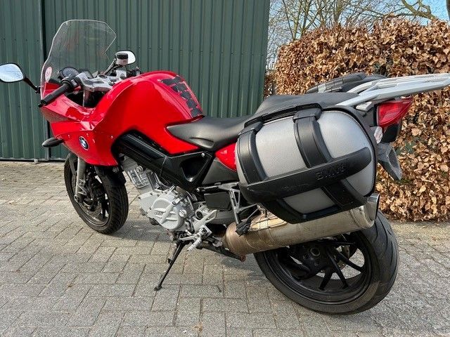 Vor einem grünen Gebäude parkt ein rotes Motorrad.