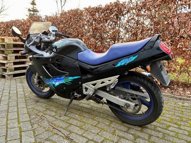 Auf einer gepflasterten Auffahrt ist ein schwarz-blaues Motorrad geparkt.