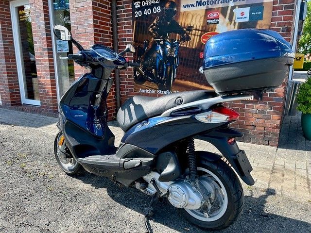 Ein blauer Motorroller ist vor einem Backsteingebäude geparkt.