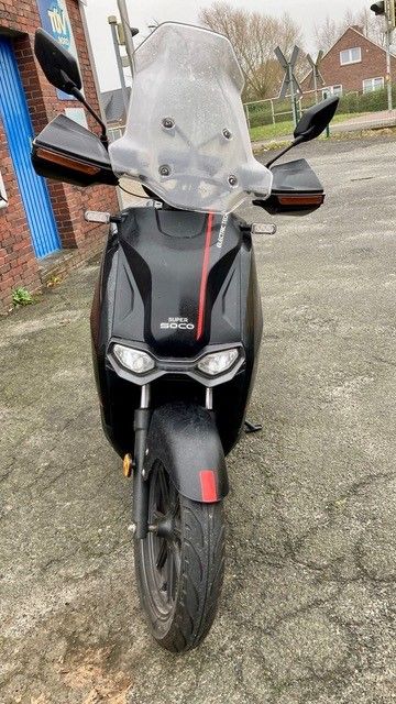 Ein schwarzer Motorroller mit Windschutzscheibe steht auf einem Parkplatz.