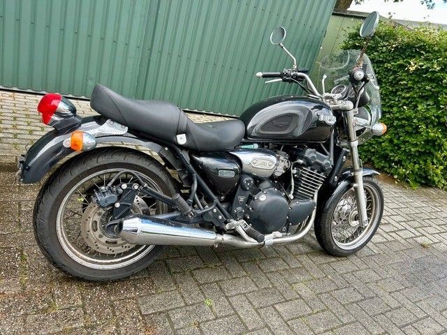 Ein schwarzes Motorrad parkte auf einer gepflasterten Auffahrt neben einer grünen Mauer und Hecke.