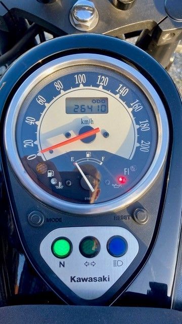 Motorrad-Armaturenbrett, Tachometer zeigt 26410 km an. Grüne Neutralanzeige leuchtet, Tankanzeige niedrig, rote Kontrollleuchte an.