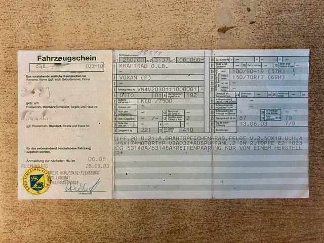 Deutsches Fahrzeugscheindokument auf beigem Untergrund mit Textfeldern und offiziellem Siegel.