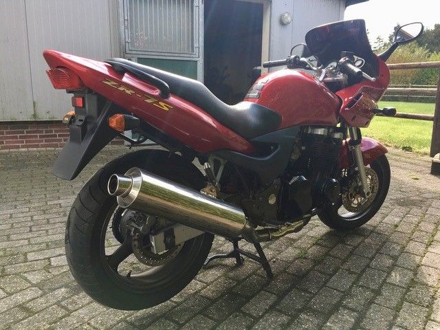 Ein rotes Motorrad ist auf einer gepflasterten Auffahrt vor einem Gebäude geparkt.
