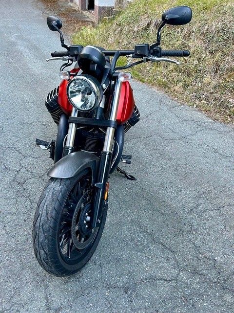 Rotes Motorrad parkt auf einer rissigen Straße, Vorderansicht mit schwarzem Lenker und silbernem Scheinwerfer.