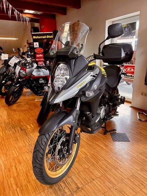 Graues Adventure-Motorrad mit Windschutzscheibe und orangefarbenen Felgen, ausgestellt in einem Showroom