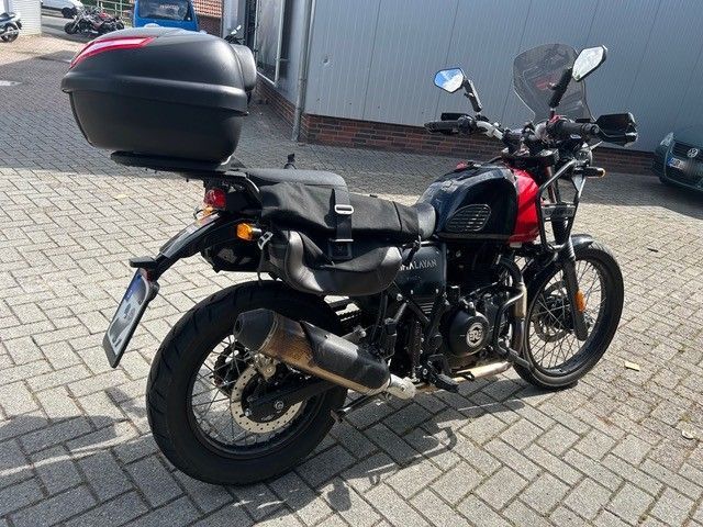 Schwarzes Motorrad mit Topcase, geparkt auf einem gepflasterten Parkplatz, Seitenansicht.