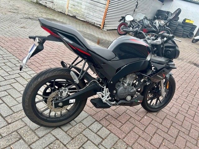 Ein schwarzes Sportmotorrad parkt auf einem gepflasterten Weg; im Hintergrund sind weitere Motorräder zu sehen.