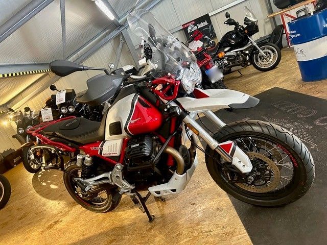 Ein rot-weißes Adventure-Motorrad steht in einer Garage, im Hintergrund sind weitere Motorräder zu sehen.