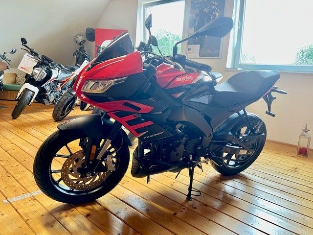 Ein rot-schwarzes Sportmotorrad steht in einem Innenraum auf einem Holzboden in der Nähe eines Fensters.