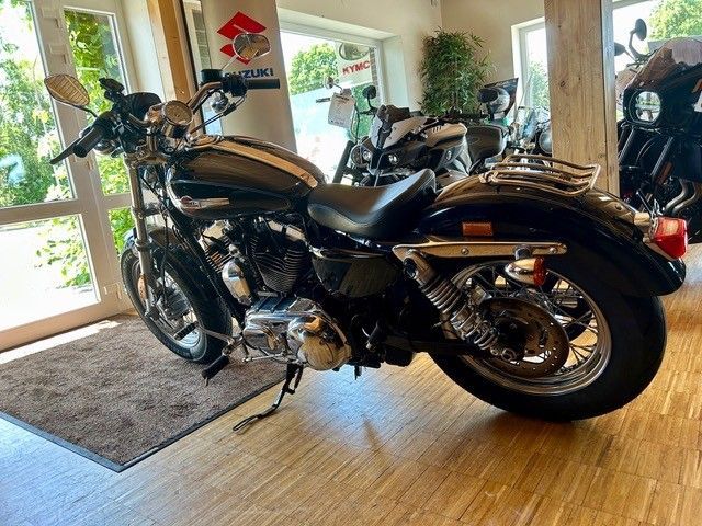 Schwarzes Motorrad parkt in einem Innenraum in der Nähe großer Fenster und einer Glastür auf gefliestem Boden.