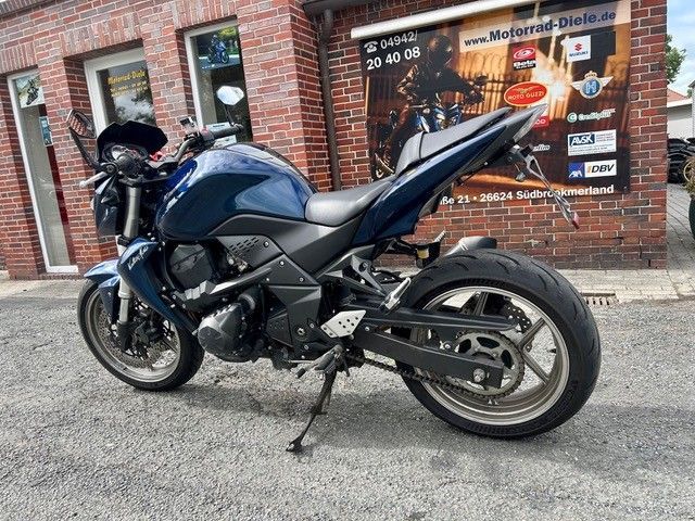 Ein dunkelblaues Sportmotorrad parkt auf einer mit Ziegelsteinen gepflasterten Straße vor einem Ladenlokal.