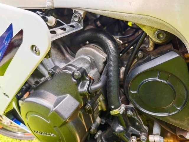 Nahaufnahme eines Motorradmotors mit schwarzen Schläuchen und Gehäuse, weißen Karosserieteilen.