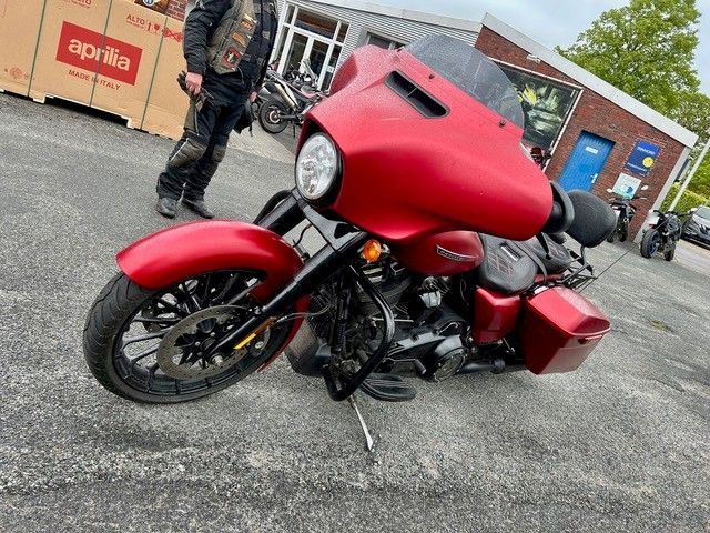 Ein rotes Tourenmotorrad steht im Freien auf dem Gelände eines Autohauses; eine Person steht daneben.