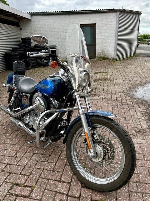 Blaues Harley-Davidson-Motorrad mit klarer Windschutzscheibe auf einer Ziegelfläche geparkt.