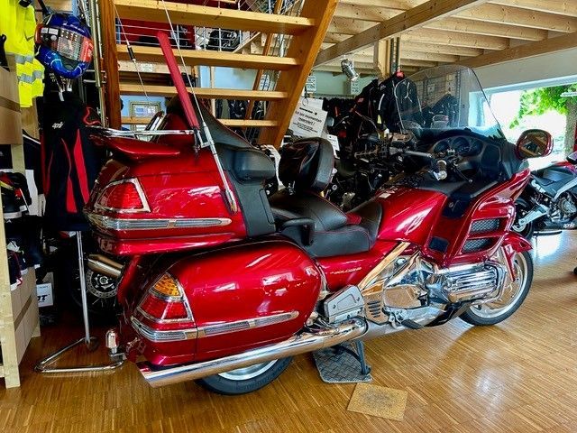 Rotes Honda Gold Wing-Motorrad im Innenbereich geparkt. Holzboden, Treppe im Hintergrund, andere Artikel im Geschäft.