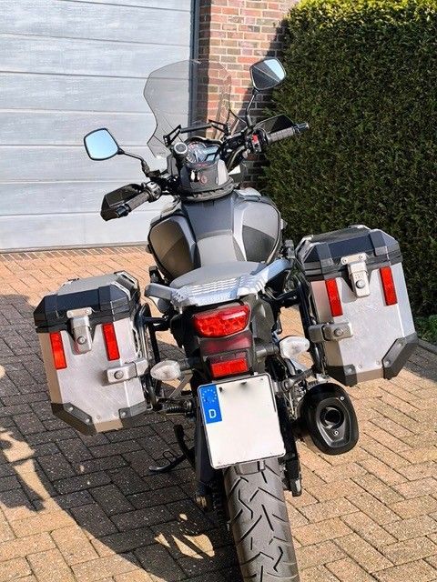 Motorrad mit silbernen Seitenkoffern und getönter Windschutzscheibe, geparkt auf einer gepflasterten Auffahrt.