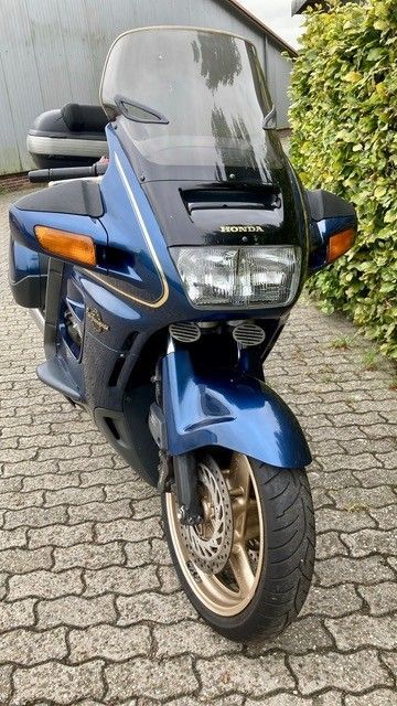 Blaues Honda ST1100-Motorrad auf einer Kopfsteinpflasterstraße geparkt. Goldene Räder, Verkleidung und große Windschutzscheibe sind sichtbar.