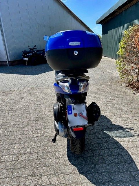 Ein blauer Roller steht auf einer gepflasterten Auffahrt