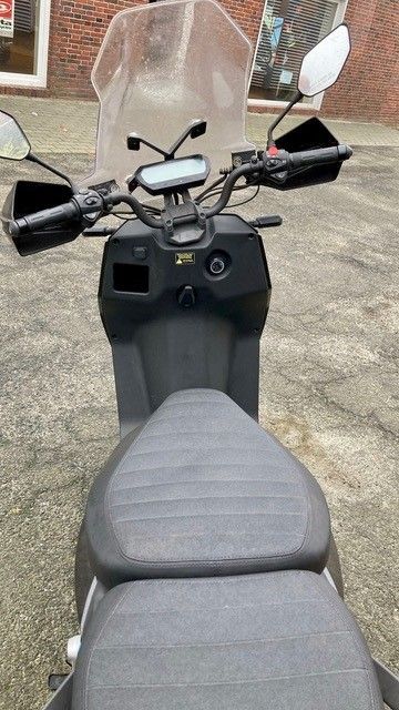 Ein schwarzer Motorroller mit Windschutzscheibe ist vor einem Backsteingebäude geparkt.