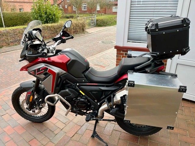 Auf einem gepflasterten Gehweg ist ein rot-schwarzes Motorrad geparkt.