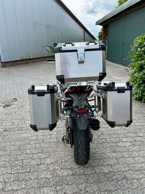 Auf einer gepflasterten Auffahrt vor einer Garage ist ein Motorrad geparkt.
