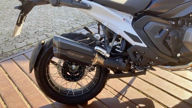 Auf einem Holzdeck ist ein schwarz-weißes Motorrad geparkt.