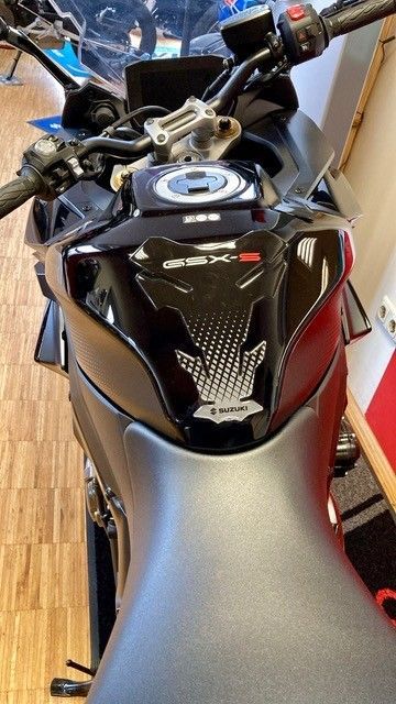 Schwarzer Motorrad-Benzintank mit Tankschutz in einem Ausstellungsraum.