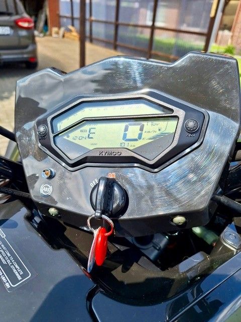 Armaturenbrett eines schwarzen Motorrads mit beleuchteter Digitalanzeige und Geschwindigkeitsanzeige 0. Schlüssel eingesteckt und gedreht, Tankanzeige niedrig.