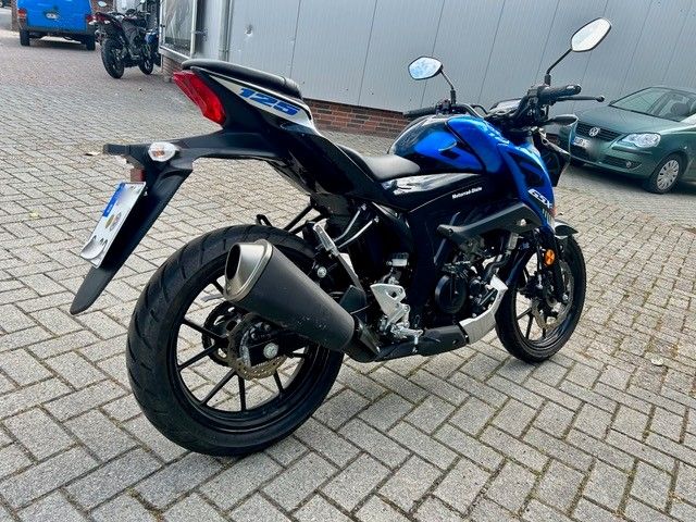 Ein blau-schwarzes Motorrad parkte auf einer mit Ziegelsteinen gepflasterten Straße in der Nähe von Autos und einem Gebäude.