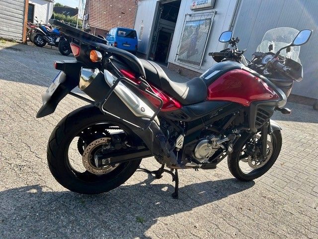 Ein rot-schwarzes Sportmotorrad parkt auf einer gepflasterten Straße in der Nähe eines Gebäudes.