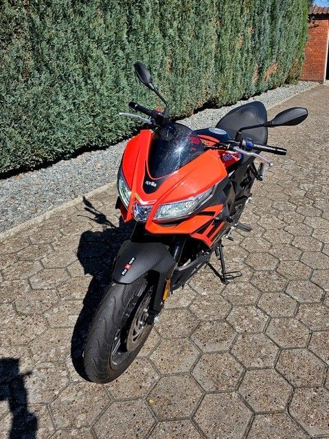 Auf einem gepflasterten Gehweg ist ein rot-schwarzes Motorrad geparkt.