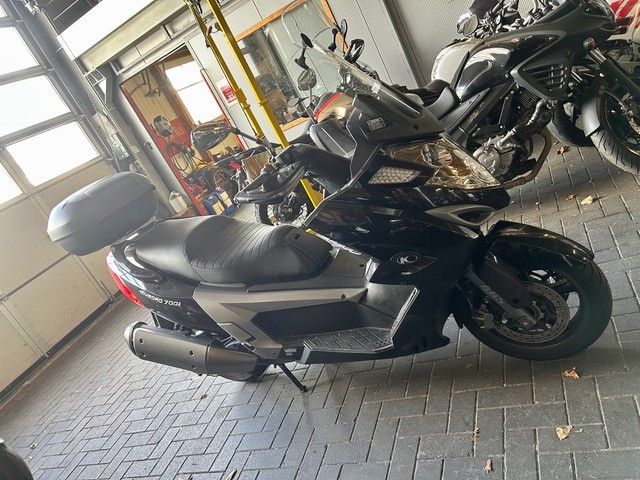 Schwarzer Roller mit Topcase und glänzender Verkleidung steht in einer Garage neben anderen Motorrädern.