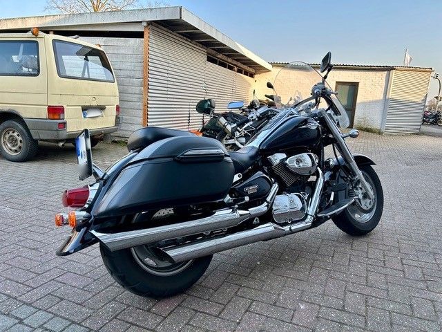 Auf einem Parkplatz steht neben einem gelben Lieferwagen ein schwarzes Motorrad.