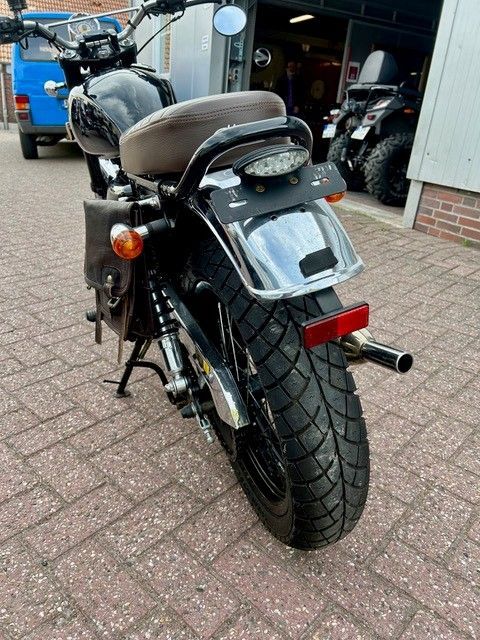 Rückansicht eines schwarzen Motorrads, das auf einer gepflasterten Auffahrt vor einer Garage geparkt ist.
