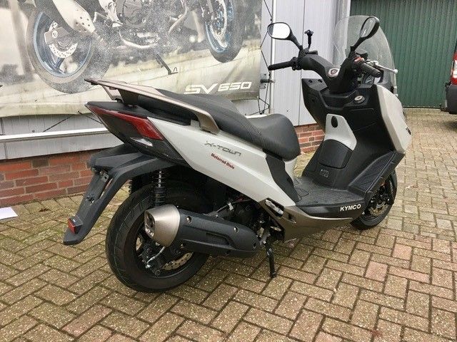 Ein weißer Motorroller ist auf einer gepflasterten Auffahrt vor einem Gebäude geparkt.