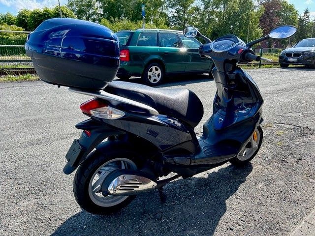 Ein Motorroller mit einem blauen Kasten auf der Rückseite steht auf einem Parkplatz.
