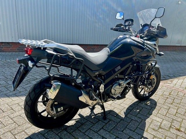 Ein blau-schwarzes Motorrad parkt auf einem Ziegelpflaster neben einer Wellblechwand.