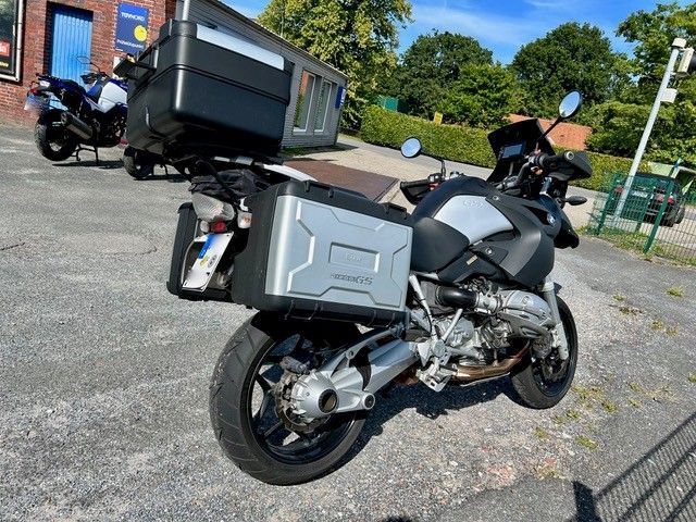 Schwarz-silbernes Motorrad mit Seiten- und Dachgepäck im Freien geparkt.
