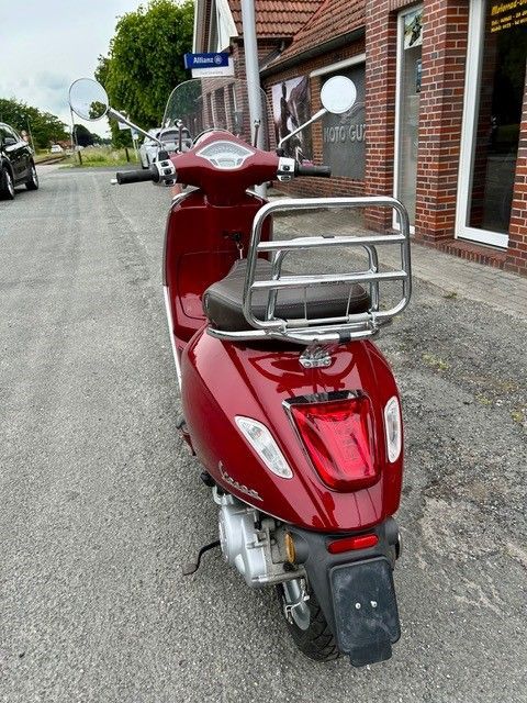 Ein roter Motorroller parkt am Straßenrand vor einem Backsteingebäude.