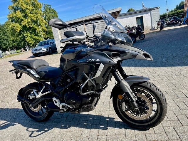 Schwarzes Tourenmotorrad mit Windschutzscheibe und Topcase parkt bei Tageslicht auf einem gepflasterten Parkplatz.