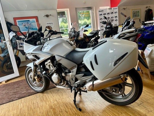 Weißes Sportmotorrad in einem Ausstellungsraum, im Hintergrund weitere Motorräder.